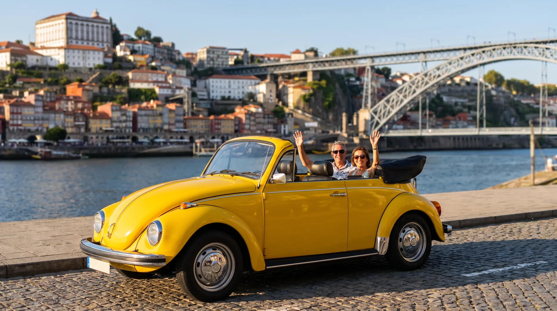 Yellow Volkswagen Beetle convertible driving along Porto's Ribeira riverfront with the Dom Luís I bridge and colourful houses in the background